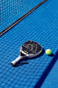 pexels-marcia-salido-346903577-31012869 | Real World Fitness - Nottingham Gym, Personal Training and Sports Massage Close-up of a paddle tennis racket and two tennis balls on a bright blue court with a net in the background.